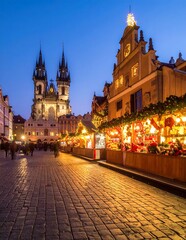 Obraz premium Historic Church Towers Over Illuminated Christmas Market Stalls in Old Town Square