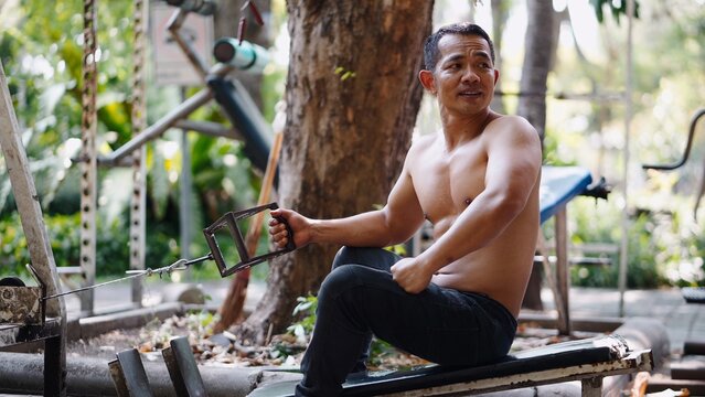 Asian man building strength outdoors, pulling cable on street workout machine