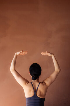 Woman Doing Stretching Exercise Against Brown Wall