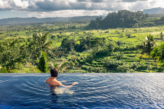 Man relaxing in infinity pool overlooking tropical rice terraces 