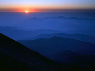 Fototapeta premium Misty, layered mountains fade into a soft, golden sunrise