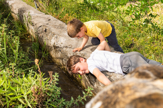 Boys curiously exploring running water in concrete ditch