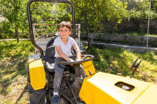 Boy smiling driving yellow tractor in rural garden