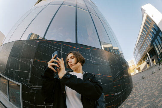 Young Person Using Smartphone Near Modern Building in City