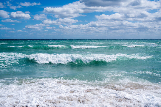 Turquoise waves meet sky under fluffy clouds
