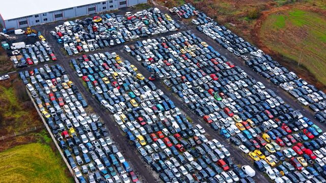 Wide angle drone view of massive automotive salvage yard. High angle panoramic shot of thousands of damaged and old cars stored next to industrial warehouse building.