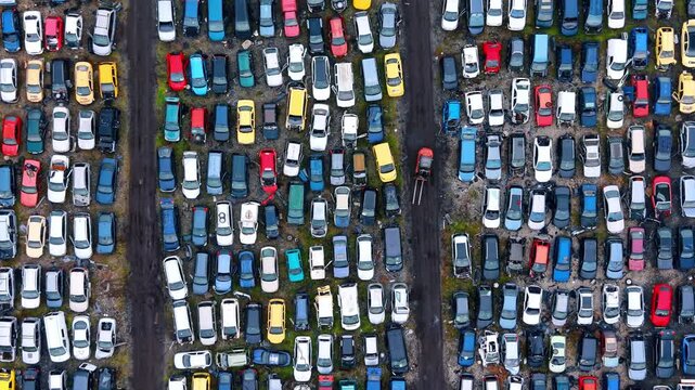 Straight down aerial perspective of vehicle recycling lot. Top down symmetrical shot of colorful cars parked in vertical columns with a small forklift operating.