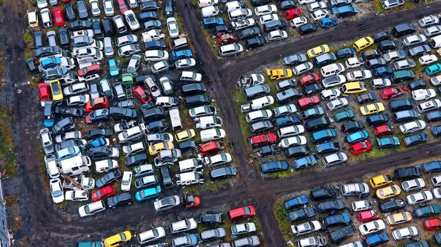 Aerial view of organized rows of vehicles at scrapyard. High angle shot showing multi colored cars parked in strict lines at a recycling facility.
