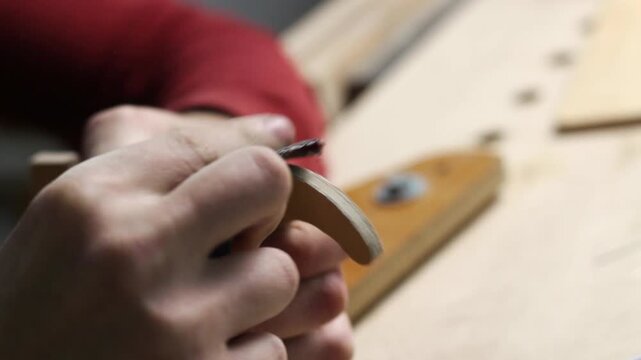 Close-up of a craftsman hands processing a small wooden part in a workshop. Carpenter working on detail customization with selective focus
