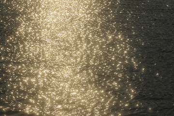 Abstract golden bokeh dancing on a dark water surface under summer sunlight. A premium natural background ideal for wellness, luxury and inspirational design.