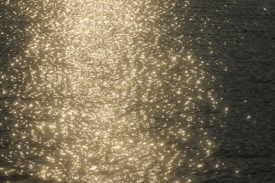 Abstract golden bokeh dancing on a dark water surface under summer sunlight. A premium natural background ideal for wellness, luxury and inspirational design.