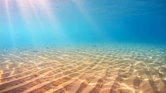 Underwater ocean scene with sunlight shining on sandy seabed and clear blue water