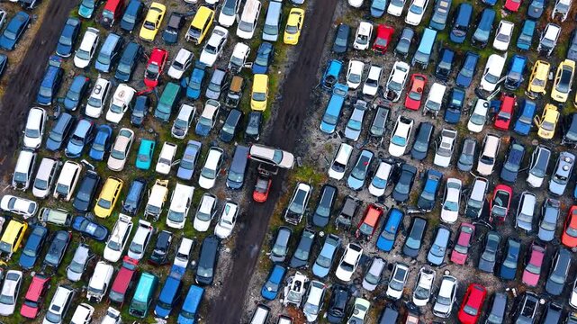 Overhead drone shot of automotive junkyard and forklift. Sorted scrap cars with a forklift lifting a vehicle frame on a dirt road.