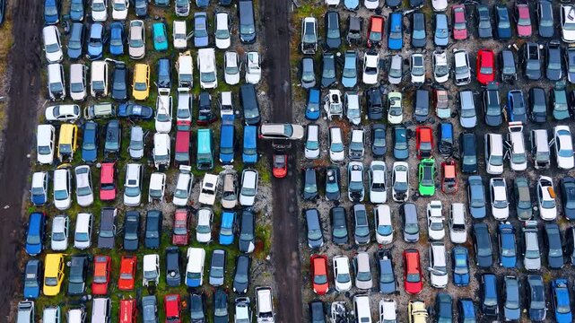 Daytime cars in a big lot. Many cars are parked close together in a lot. The scene shows a variety of colors and types of vehicles.
