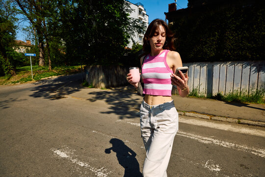 Casual young woman crosses the street, looking at a mobile phone