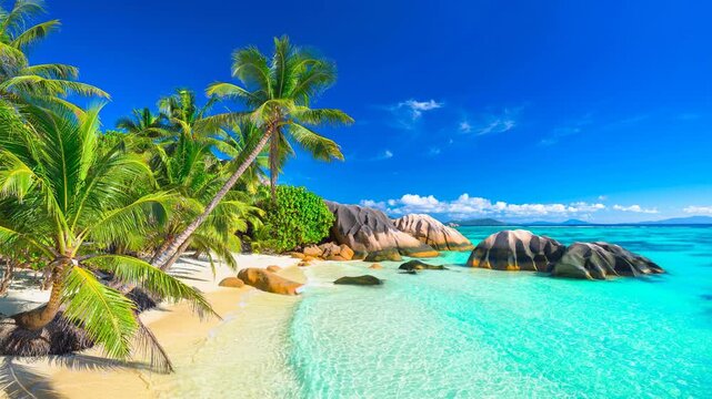 Tropical beach with clear turquoise water palm trees and large granite rocks under blue sky