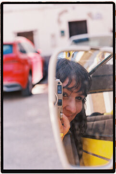 Woman capturing reflection in car mirror