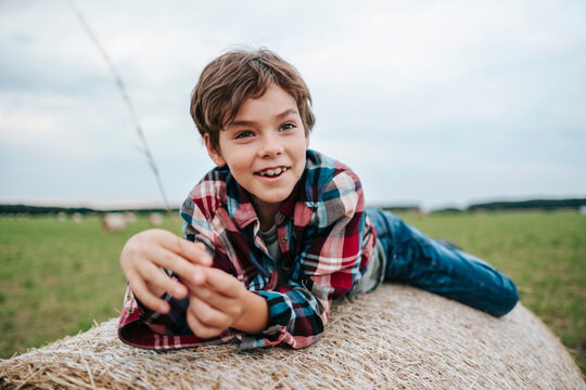 Smiling Boy Relaxes on a Hay Bale in a Sunny Field
