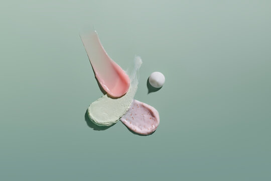 Swatches of pink and green cosmetic creams and scrubs on green