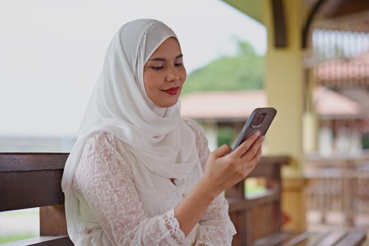 Asian person in a cream hijab using a phone at a pavilio