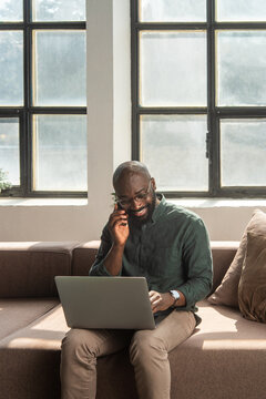 Smiling Man Working Remotely on Laptop and Phone in Bright Workplace