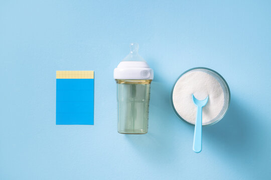 Baby bottle with formula powder and spoon on a blue background
