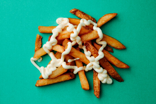 a pile of french fries with mayonnaise on a green background