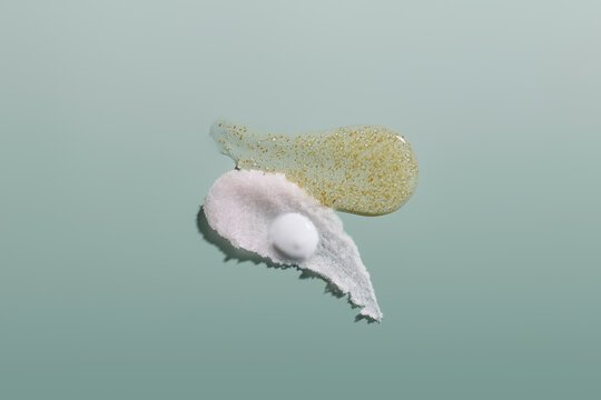 Swirls of cosmetic textures including scrub, serum, and cream on green