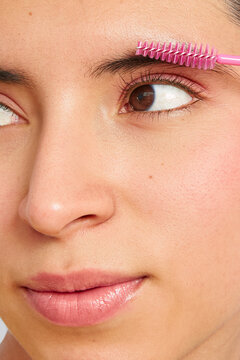 Young woman grooming eyebrows with pink spoolie brush