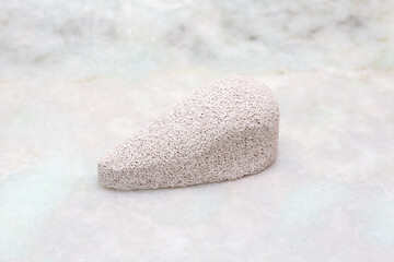 Pumice stone with a smooth surface and tapered shape, placed on a light marble background, showcasing its porous texture and natural color variations © Nizoli