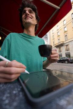 Gen Z guy enjoying coffee while working on tablet in Italy