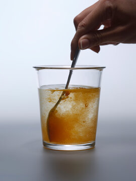 Hand stirring a golden liquid in a clear glass with a metal spoon