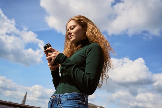 Woman Using Mobile Phone Outdoors Under Blue Sky With Clouds