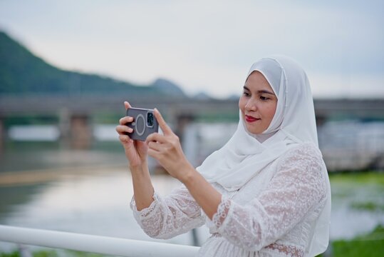 Asian person in a cream hijab taking a photo with a phon