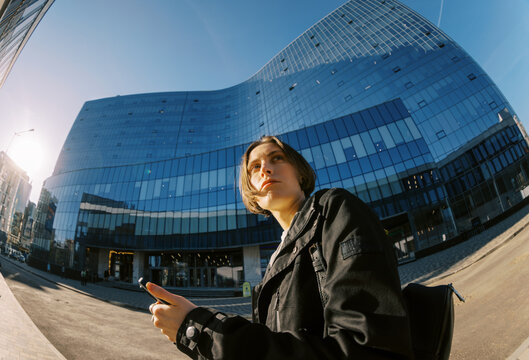 Woman Stands Outside a Modern Building While Using a Smartphone