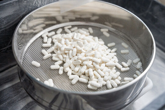 White pills sifting in a metal sieve
