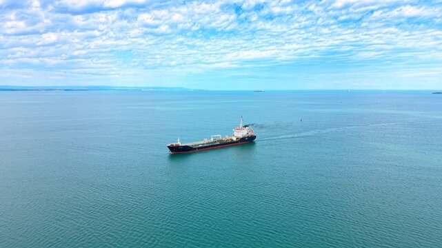 Cargo ship moves across blue sea water. A cargo ship sails through calm blue waters under a cloudy sky during the day. The scene shows the vast ocean.