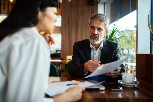 Mature businessman advising client over paperwork in cafe