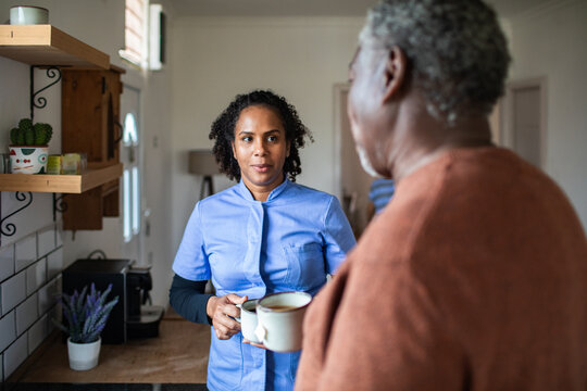 Home caregiver serving coffee to senior man in kitchen