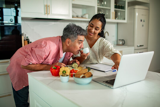 Couple preparing vegetables and checking recipes on laptop in modern kitchen
