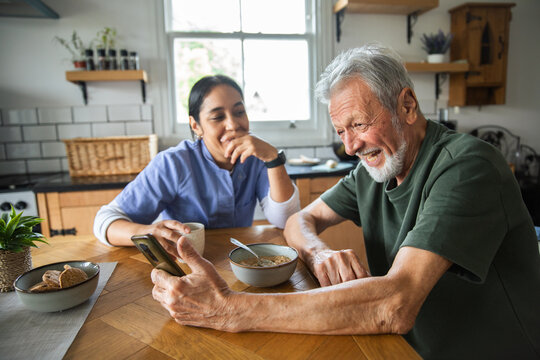 Senior man and woman laughing over smartphone at home kitchen table