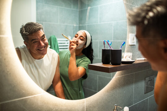 Happy couple applying facial mask in home bathroom mirror