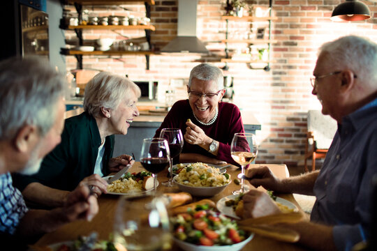 Senior friends laughing over dinner in home kitchen