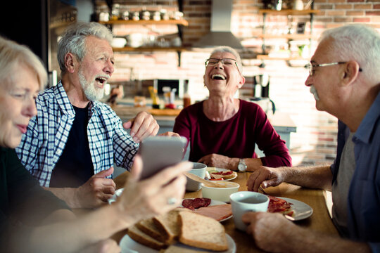 Senior friends laughing over breakfast at home kitchen