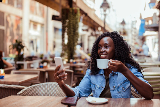 Smiling woman drinking coffee and using smartphone at outdoor cafe