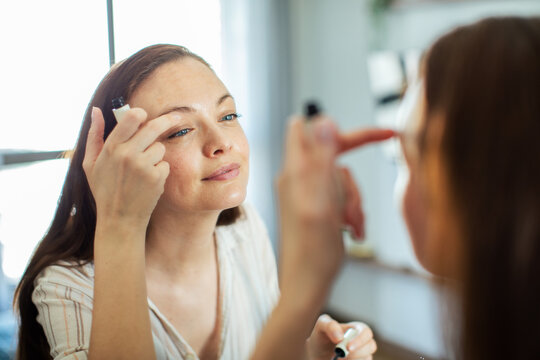 Smiling woman applying eye cream at home mirror