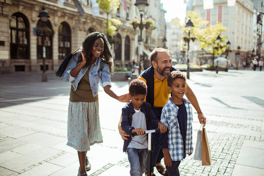 Family shopping and riding scooter on sunny city street