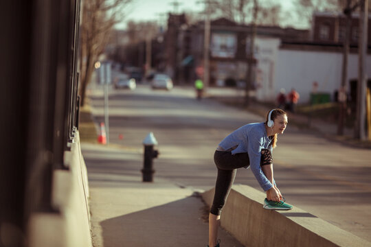 Young woman lacing running shoes on city sidewalk