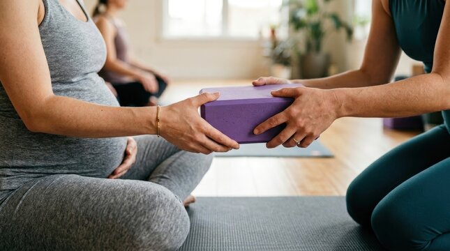 Yoga instructor handing block to pregnant woman during prenatal class