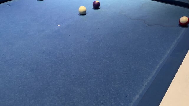 Skilled player executing a precise shot in a game of billiards. The white cue ball strikes the purple ball on the blue cloth table